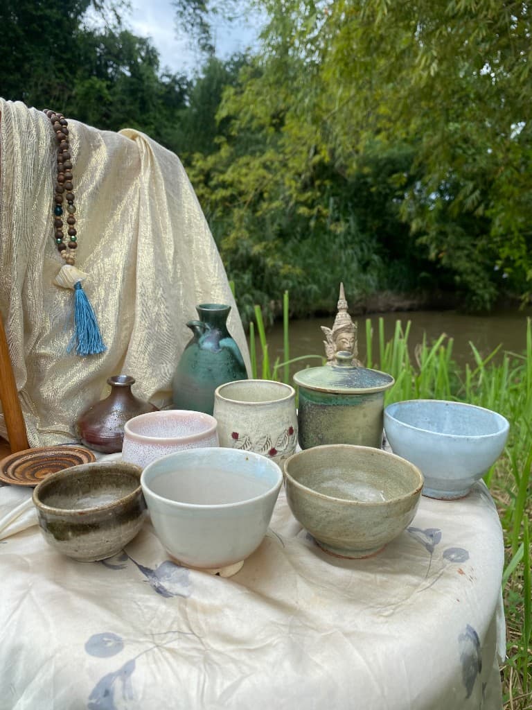 Handmade cups, a lidded jar and teapots on a table by the water