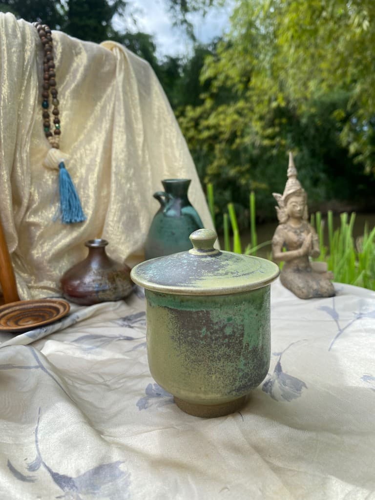 Moss-green lidded cup among garden ceramics
