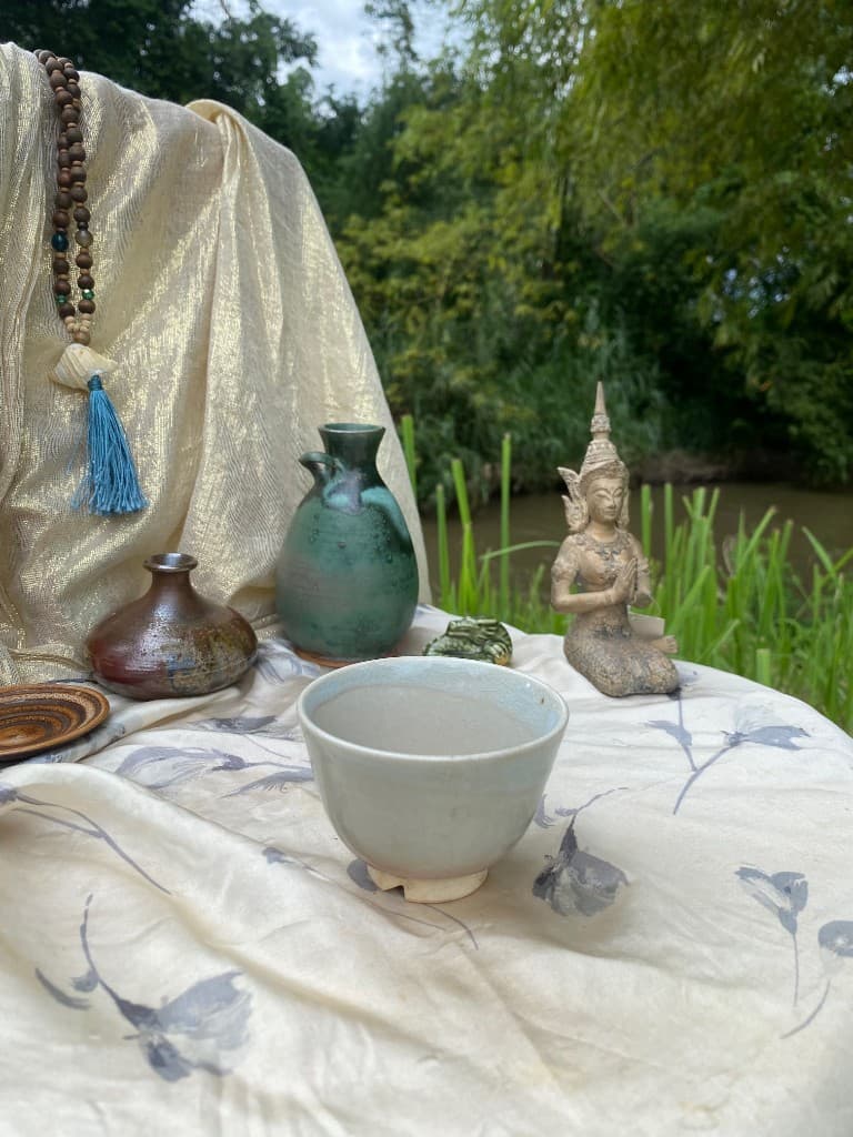 Pale tea bowl with green and bronze vessels by the river