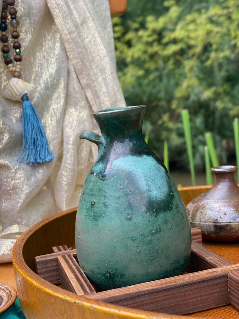 Seafoam and dark-glaze ceramic carafe on a wooden tray